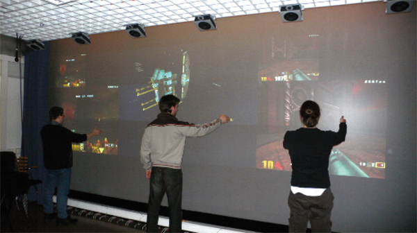 Two persons playing Q3A and one person playing Homeworld simultaneously on a 7x4 tile display wall. Q3A runs on 2x2 tiles to the left and right, and Homeworld on 3x3 tiles in the middle.